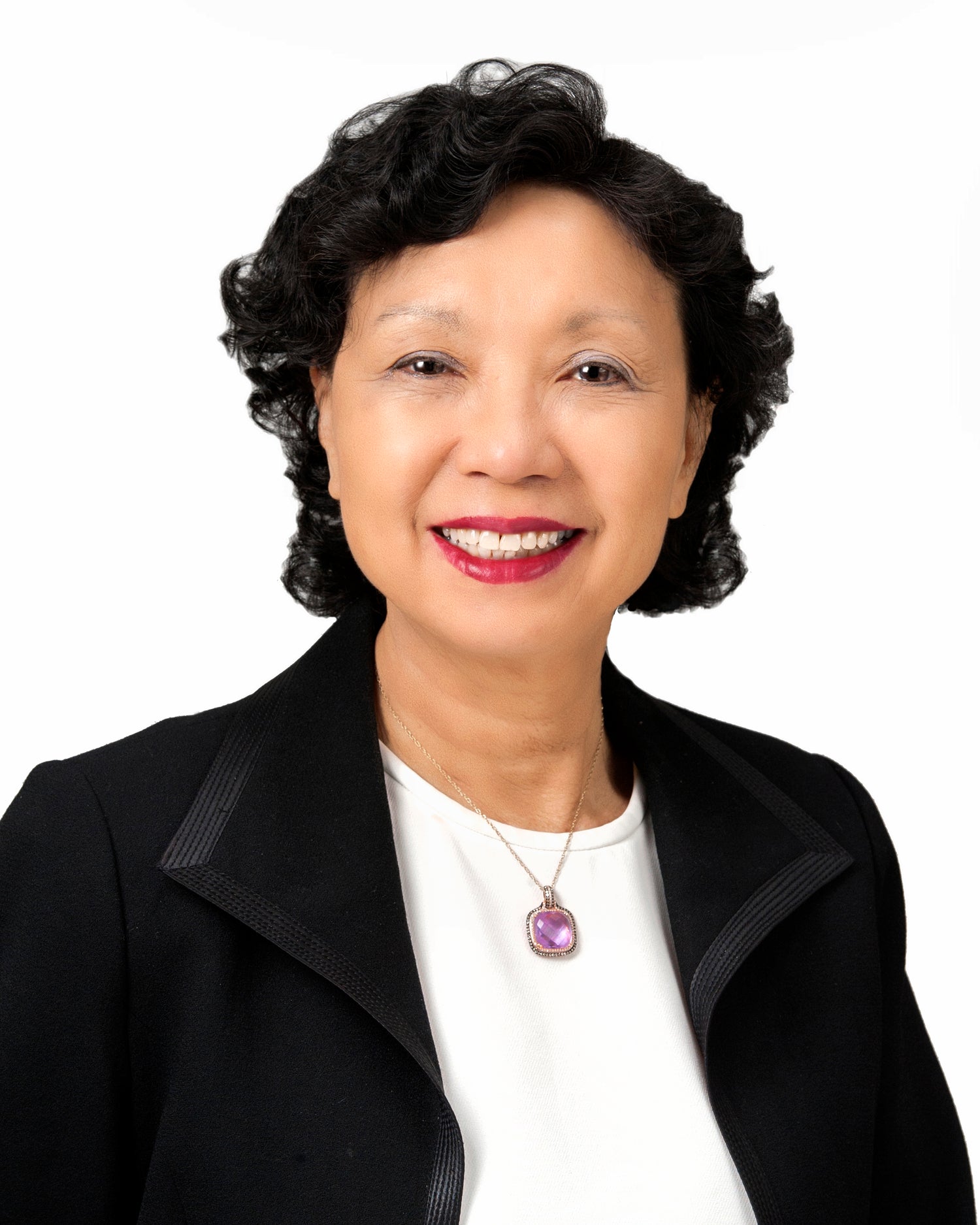 Woman wearing a black blazer over a white shirt with a visible necklace on a white background